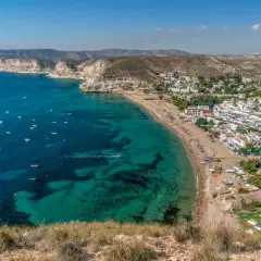 Costa blanca con pueblo blanco y mar turquesa. El agua amarga del Mediterráneo baña la playa, salpicada de barcas.