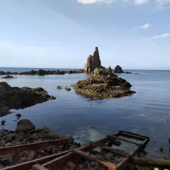 Rocas emergiendo del mar azul, como un **arrecife de las sirenas**. El agua cristalina revela el fondo rocoso.