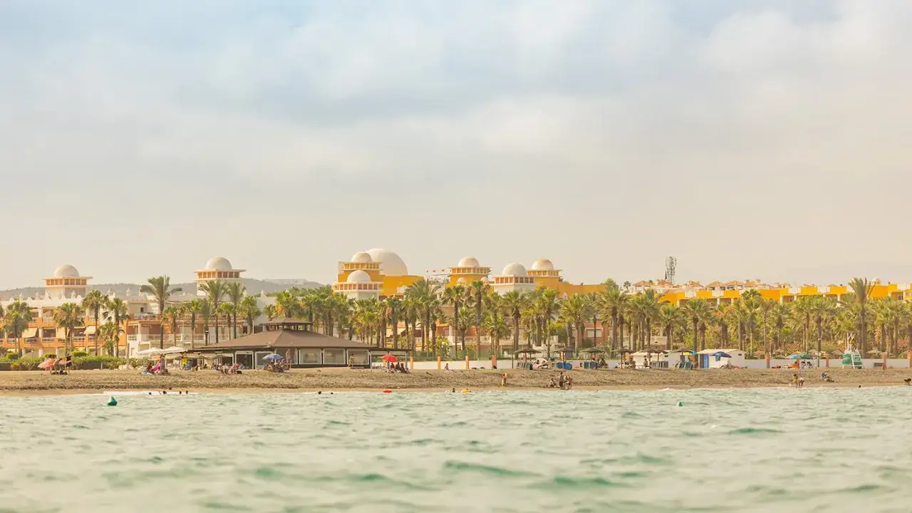 Edificios con cúpulas y palmeras en la costa. Un día perfecto para disfrutar de todo que ver en Vera, con gente en la playa y el mar.