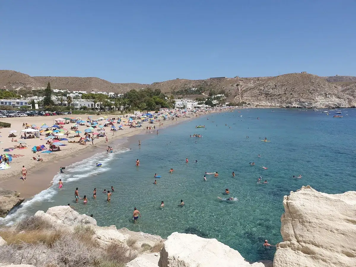 Playa abarrotada con gente disfrutando del sol y el agua clara. El mar, de un azul intenso, invita a un baño refrescante, aunque su sabor sea un poco de agua amarga.