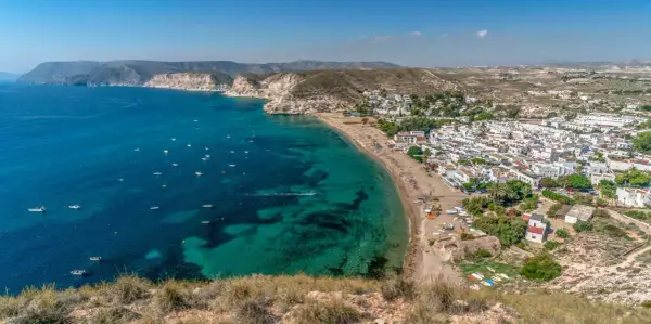 Costa blanca con pueblo blanco y mar turquesa. El agua amarga del Mediterráneo baña la playa, salpicada de barcas.